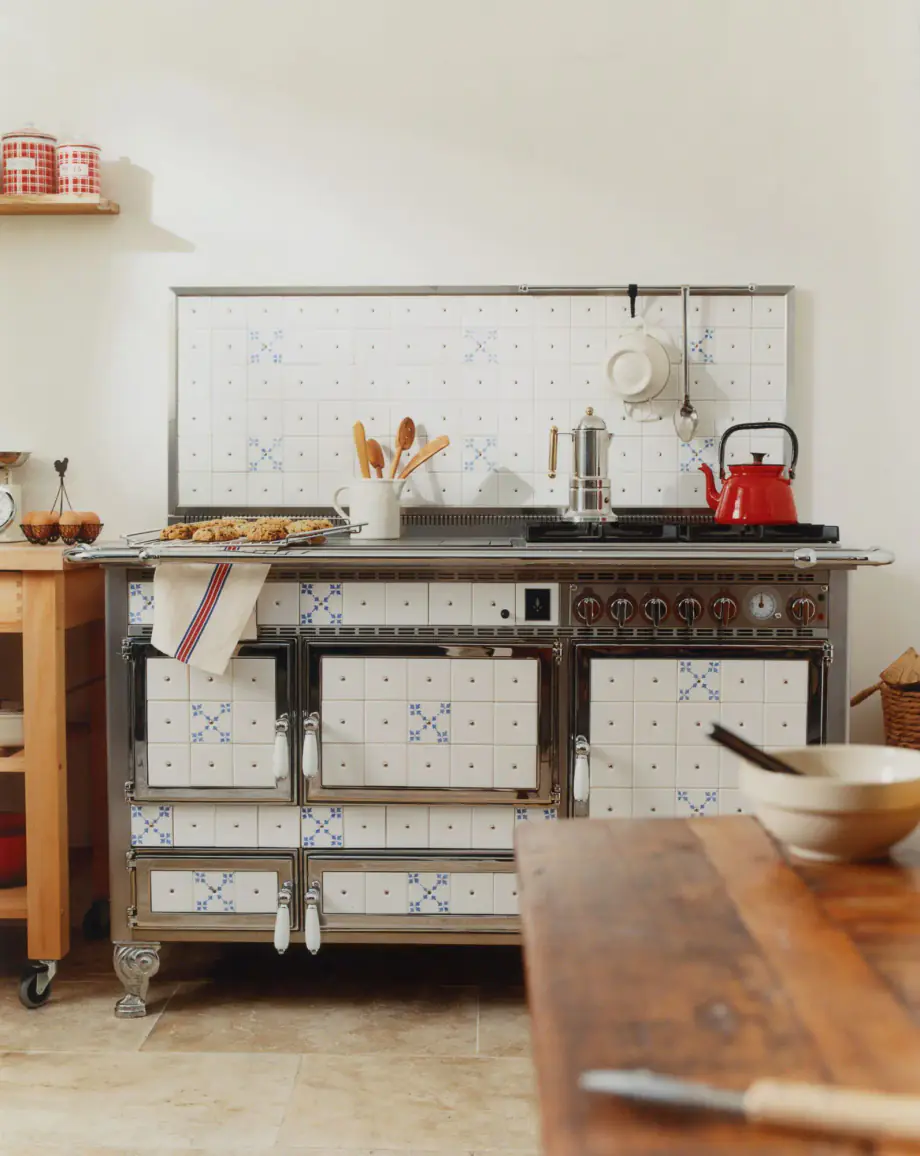 Cuisinière ancienne à motifs bleus, avec bouilloire rouge, dans une cuisine.
