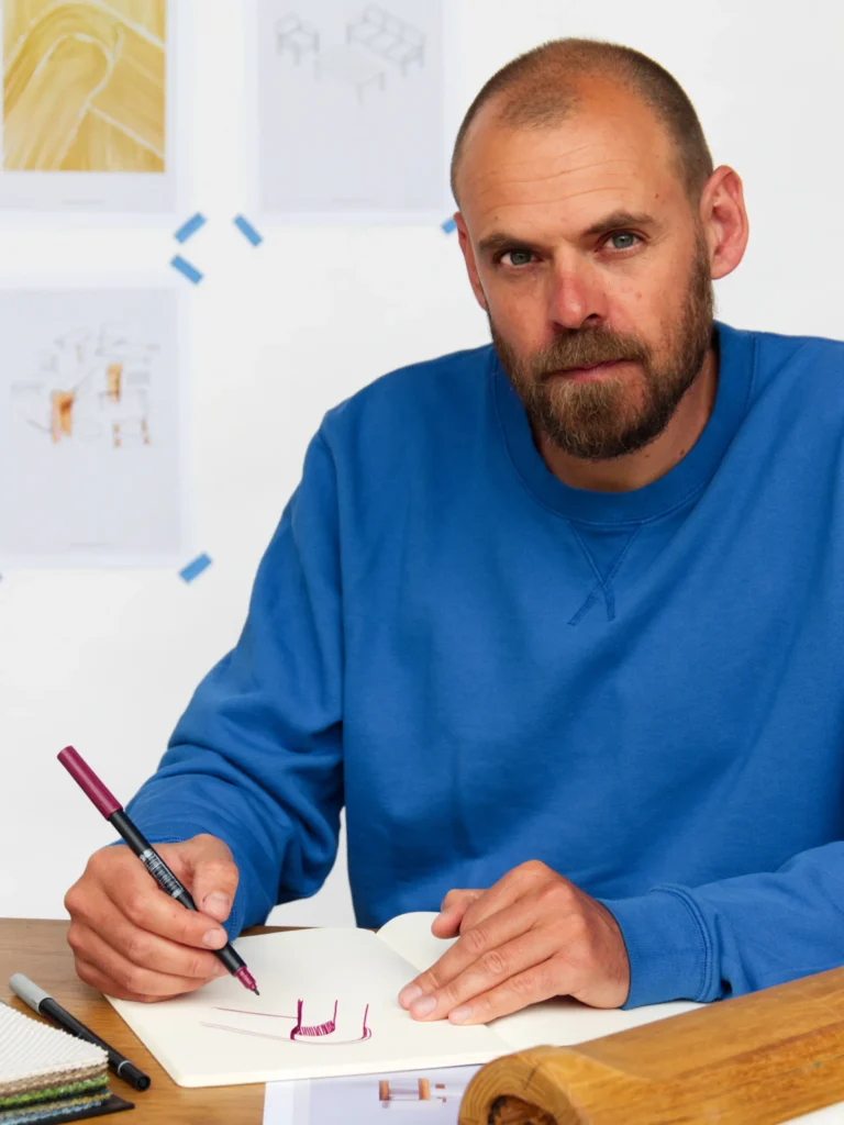 Portrait du designer en pull bleu, en train de dessiner à son bureau.