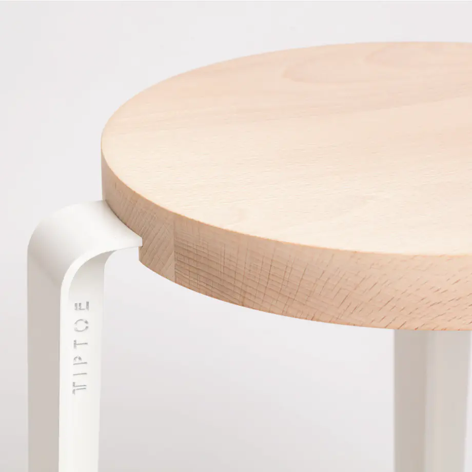 Gros plan sur le plateau rond en bois clair d'un tabouret à pieds blancs.