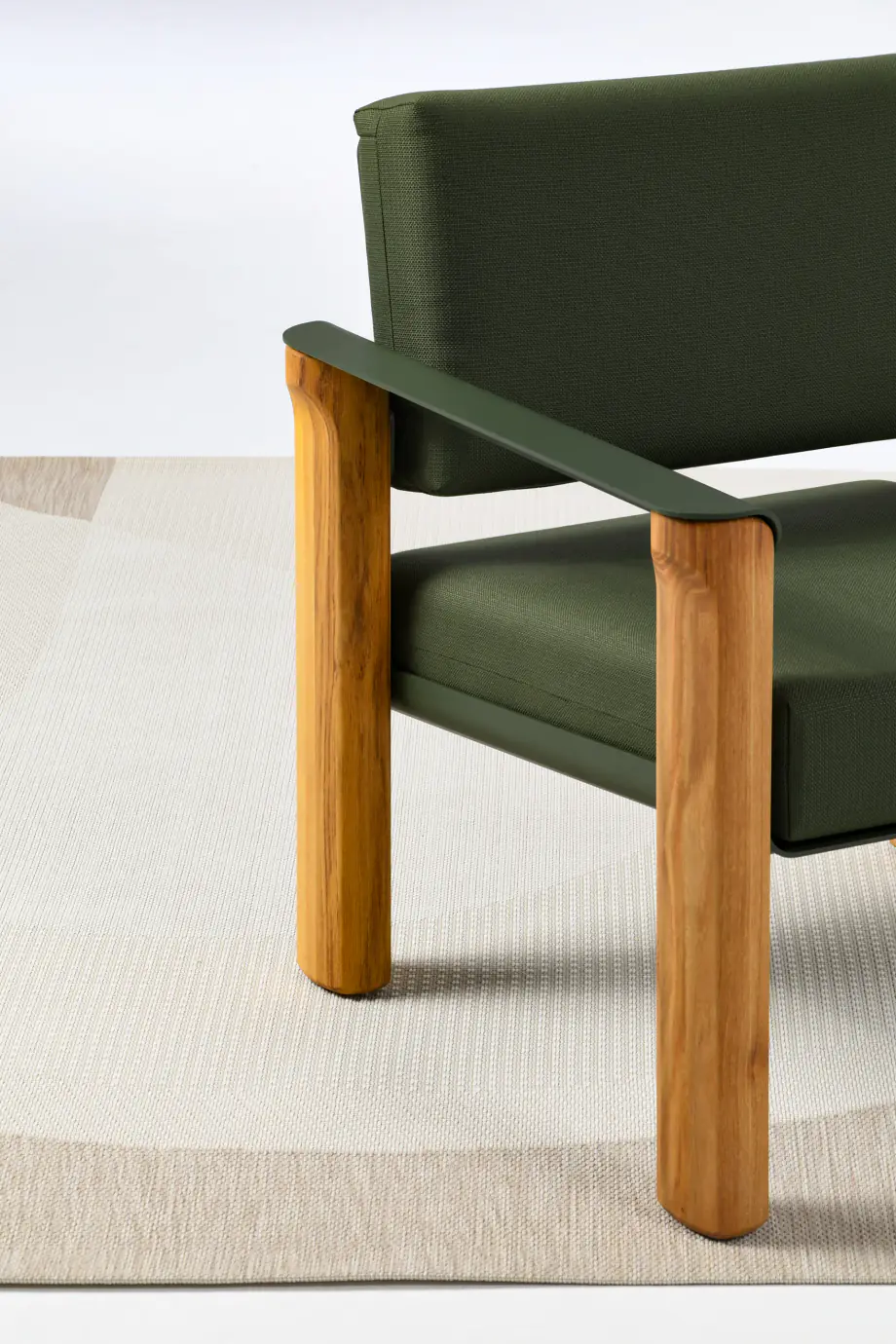Fauteuil en bois clair et tissu vert kaki, accoudoir diagonal, sur un tapis clair.
