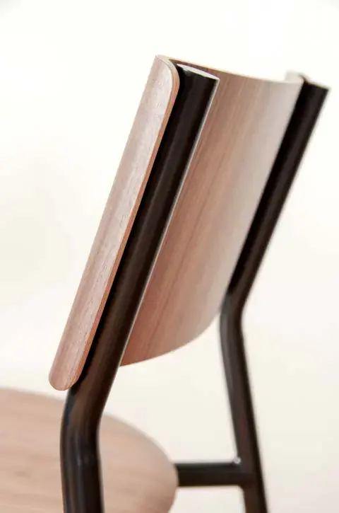 Gros plan sur le dossier courbe en bois et la structure noire d'une chaise.